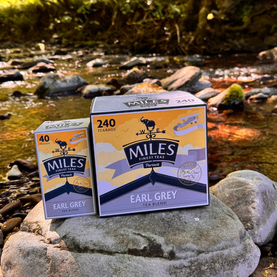 Two boxes of Miles Earl Grey tea on rocks by a stream