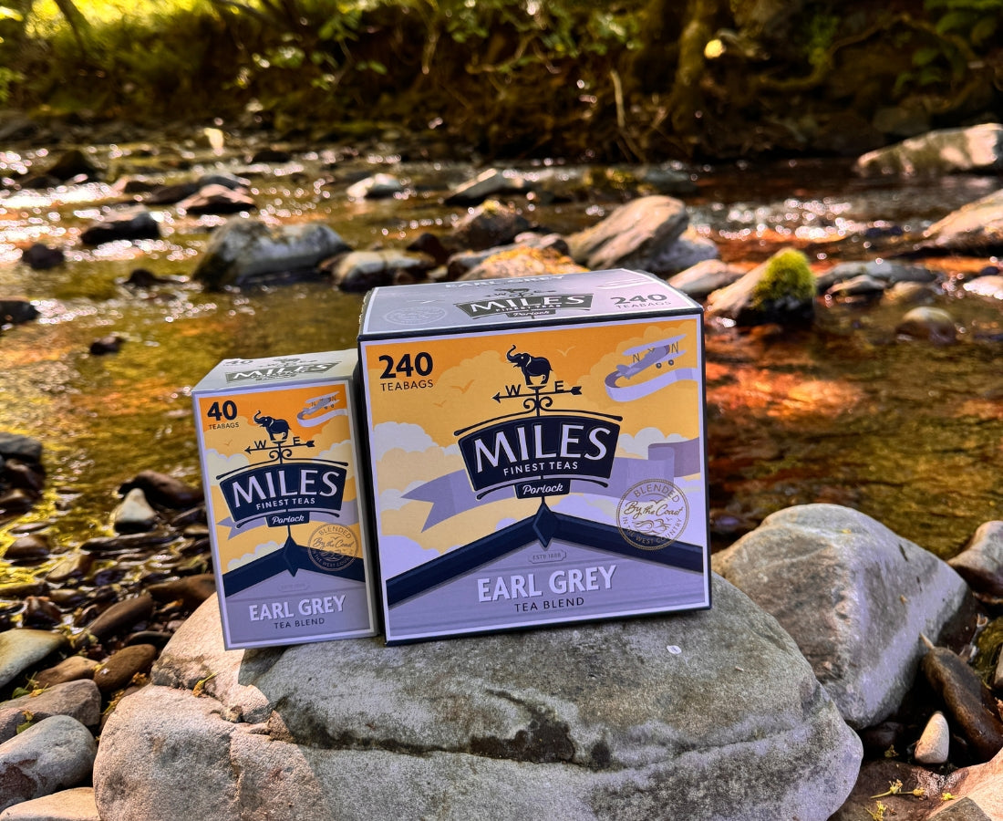 Two boxes of Miles Earl Grey tea on rocks by a stream