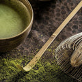 Matcha green tea bowl with whisk and spoon on a dark surface