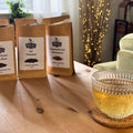 Three packages of Miles tea on a wooden table with a glass of tea in the foreground.