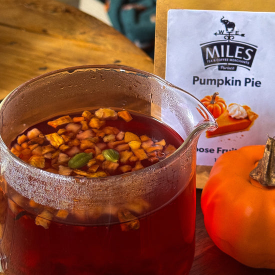 Glass of pumpkin spice tea with a pumpkin and Miles Pumpkin Pie product packaging on a wooden table.