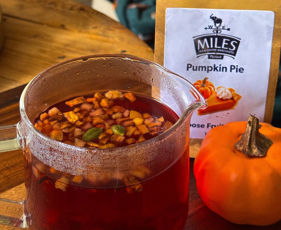 Glass of pumpkin spice tea with a pumpkin and Miles Pumpkin Pie product packaging on a wooden table.