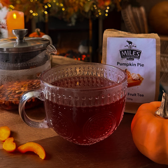 Tea cup with red liquid, pumpkin spice tea package, and small pumpkin on a wooden surface.