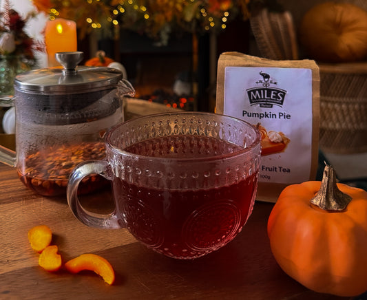 Tea cup with red liquid, pumpkin spice tea package, and small pumpkin on a wooden surface.