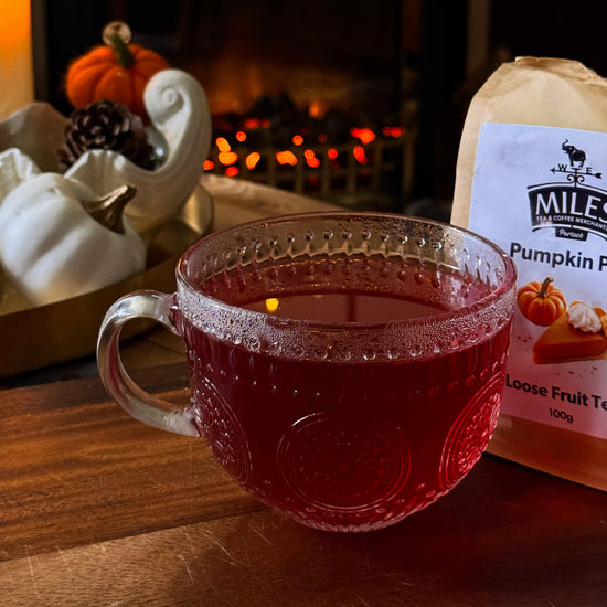 Glass mug with red liquid next to a package of Miles Pumpkin Pie tea on a wooden surface.