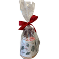 A holiday-themed gift set in a clear cellophane bag tied with a red ribbon, containing a white ceramic mug decorated with Pine Sprigs, filled with marshmallows and hot chocolate.