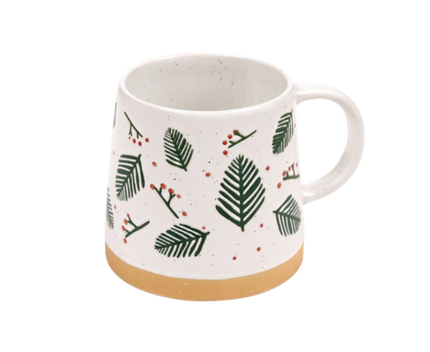 A white ceramic mug with a speckled finish, decorated with green pine leaves and small red berries, featuring a natural tan clay base and a white handle.