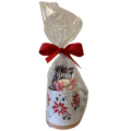 A holiday-themed gift set in a clear cellophane bag tied with a red ribbon, containing a white ceramic mug decorated with red poinsettias and green holly, filled with marshmallows and hot chocolate.