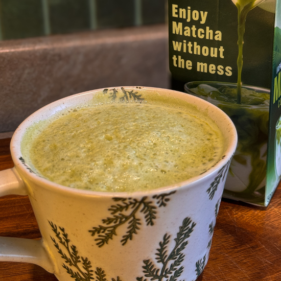 Matcha in a mug with a box of matcha mix on a wooden surface