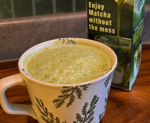 Matcha in a mug with a box of matcha mix on a wooden surface