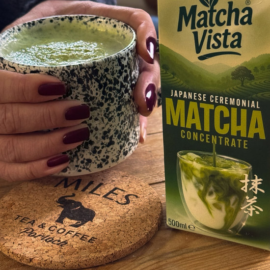 Person holding a cup of matcha green tea next to a box of Matcha Vista matcha concentrate.