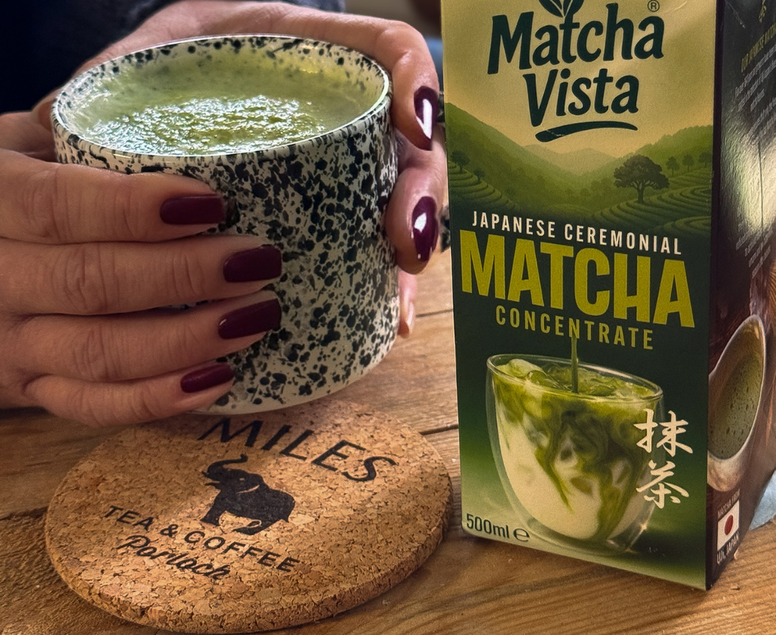 Person holding a cup of matcha green tea next to a box of Matcha Vista matcha concentrate.