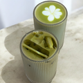 Two cylindrical glasses filled with matcha on a light surface.