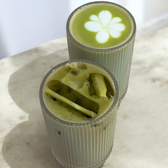Two cylindrical glasses filled with matcha on a light surface.